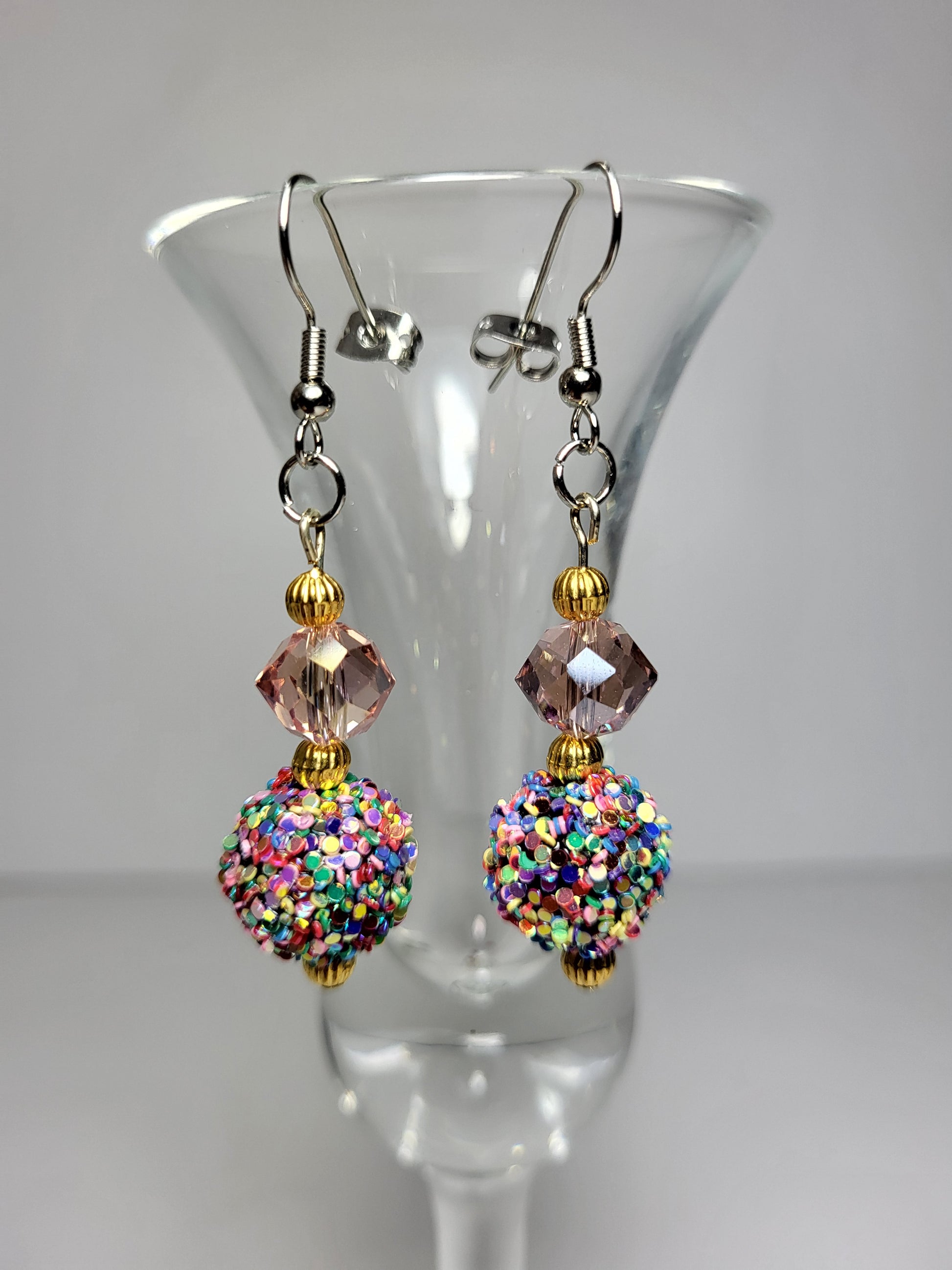 Introducing our exquisite Dazzle Dangle Earrings – a captivating blend of elegance and vibrancy that will elevate your style to new heights. These eye-catching earrings feature a stunning statement bead, meticulously adorned with a dazzling array of sparkling colors that catch the light with every movement.
