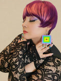 Person with colorful hair wearing a black lace top and colorful earrings.