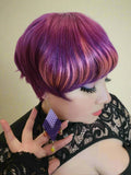Person with vibrant purple hair holding a purple earring.