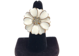 White flower-shaped earring on a black stand against a white background