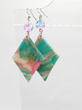A pair of handmade earrings featuring marbled green, pink, and gold resin triangles, suspended from silver hooks with iridescent pink beads.
