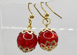 Red earrings with gold accents on a clear stand against a white background