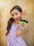 Young girl in a purple dress with floral patterns, wearing colorful scrunchies, against a beige background.