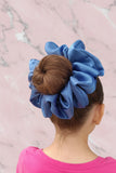 A person viewed from the back with a large blue satin scrunchie in their hair, which is styled in a bun.