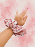Pink scrunchie on a wrist against a pink watercolor background