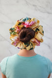 A person viewed from behind with a large, multicolored floral scrunchie in their hair.