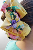 A person wearing a large yellow scrunchie with a floral pattern in their hair.