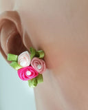 A close-up image of a hypoallergenic earring with a fabric flower design, featuring pink and green colors, attached to a titanium earring post.
