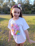 Young girl wearing a white t-shirt with a colorful graphic design outdoors.