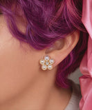 Close-up of a person wearing a floral pearl earring with pink hair.