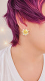 Close-up of a person wearing a yellow flower earring with purple hair.