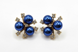 A pair of Midnight Empress Blossom Stud Earrings with blue pearls and gold-colored metalwork on a white background.