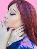 a woman with reddish brown hair wearing blue cluster earrings and bracelets.