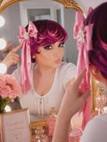 Woman with pink hair styled with a bow, looking at herself in a mirror.