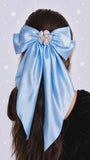 Large blue bow with decorative elements in hair against a light purple background