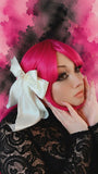 Person with bright pink hair and a large white bow against a pink and black abstract background