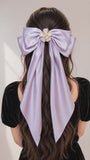 Person with long hair styled with a large purple bow and decorative flower on a plain background