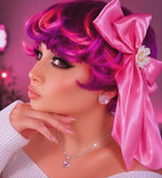 Woman with vibrant pink hair styled in an updo with a large pink bow, wearing jewelry.