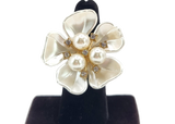 Pearl flower ring on a black stand against a white background