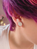 Close-up of a person wearing a sparkling earring with purple hair.