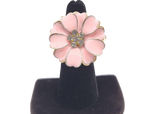 Pink flower-shaped earring on a black stand against a white background