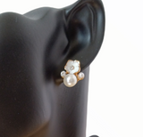 a close-up of faux pearl earrings with gold accents, rhinestones on a black mannequin. 